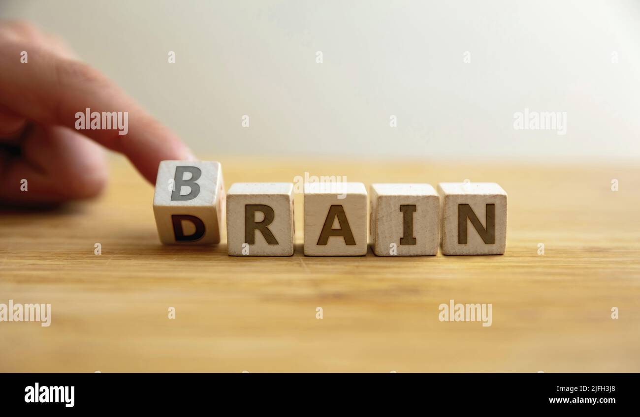 Brain drain concept. Finger flips letter at wooden cube changing the