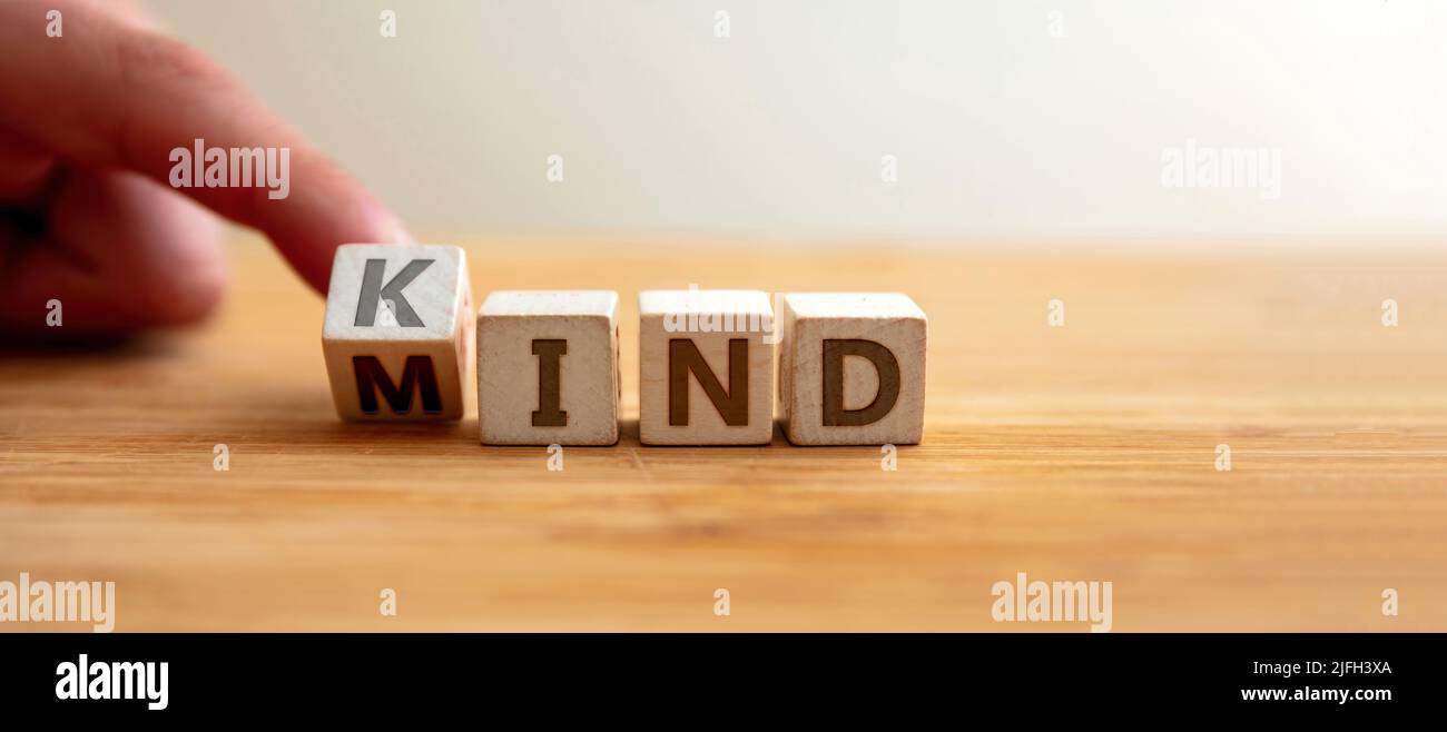 Kind mind concept. Finger flips letter at wooden cube changing the word mind to kind. Message for kindness, humanism, emotion, mental health, positive Stock Photo