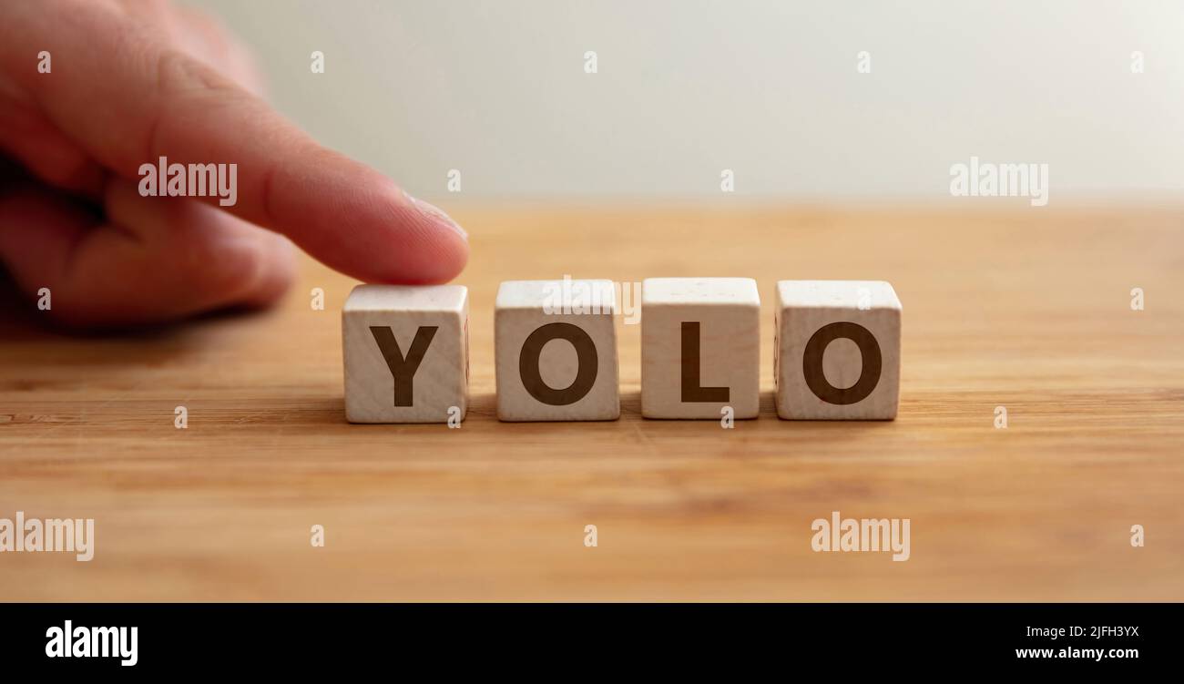Yolo concept. Word yolo on wooden cube with finger to shows letter y. You Only Live Once phrase, message to seize the day, positive lifestyle, follow Stock Photo