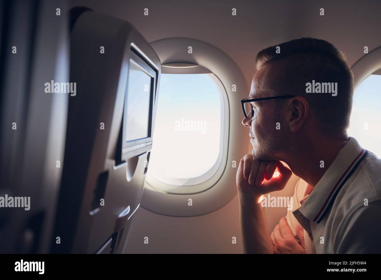 Portrait of man traveling by airplane. Passenger looking through plane window during flight Stock Photo