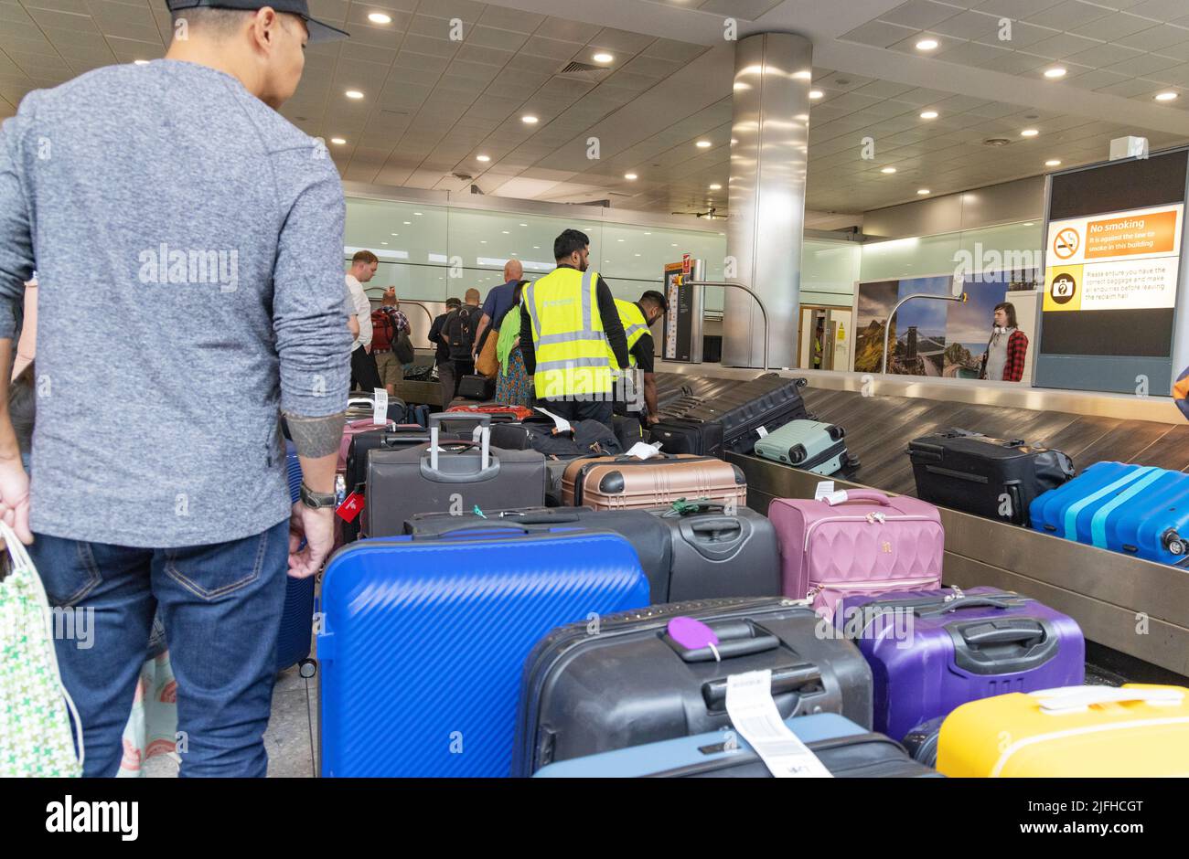 Heathrow airport delays; baggage handlers managing piles of baggage in travel chaos, Terminal 3 baggage collection, London airport UK Stock Photo