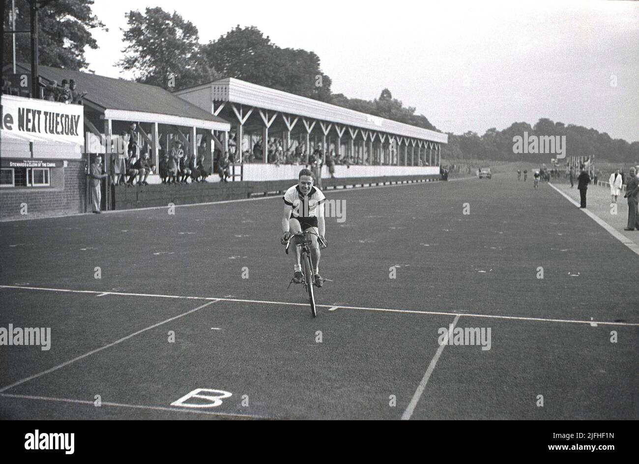 1937, historical, a racing cyclist crossing the line for a victory on the  motoring race circuit at Crystal Palace Park, South London, England, UK. The park was London’s first home of cycle racing in 1869, with its first dedicated cycle track opening in 1880. The motor racing circuit opened in the park in 1927, with motor cycle racing the first event. In 1936 the one mile circuit was extended to two miles and tarmac laid over its entire length and in 1937 the first London Grand Prix took place. Seen in the picture is the main grandstand of the motor racing circuit. Stock Photo