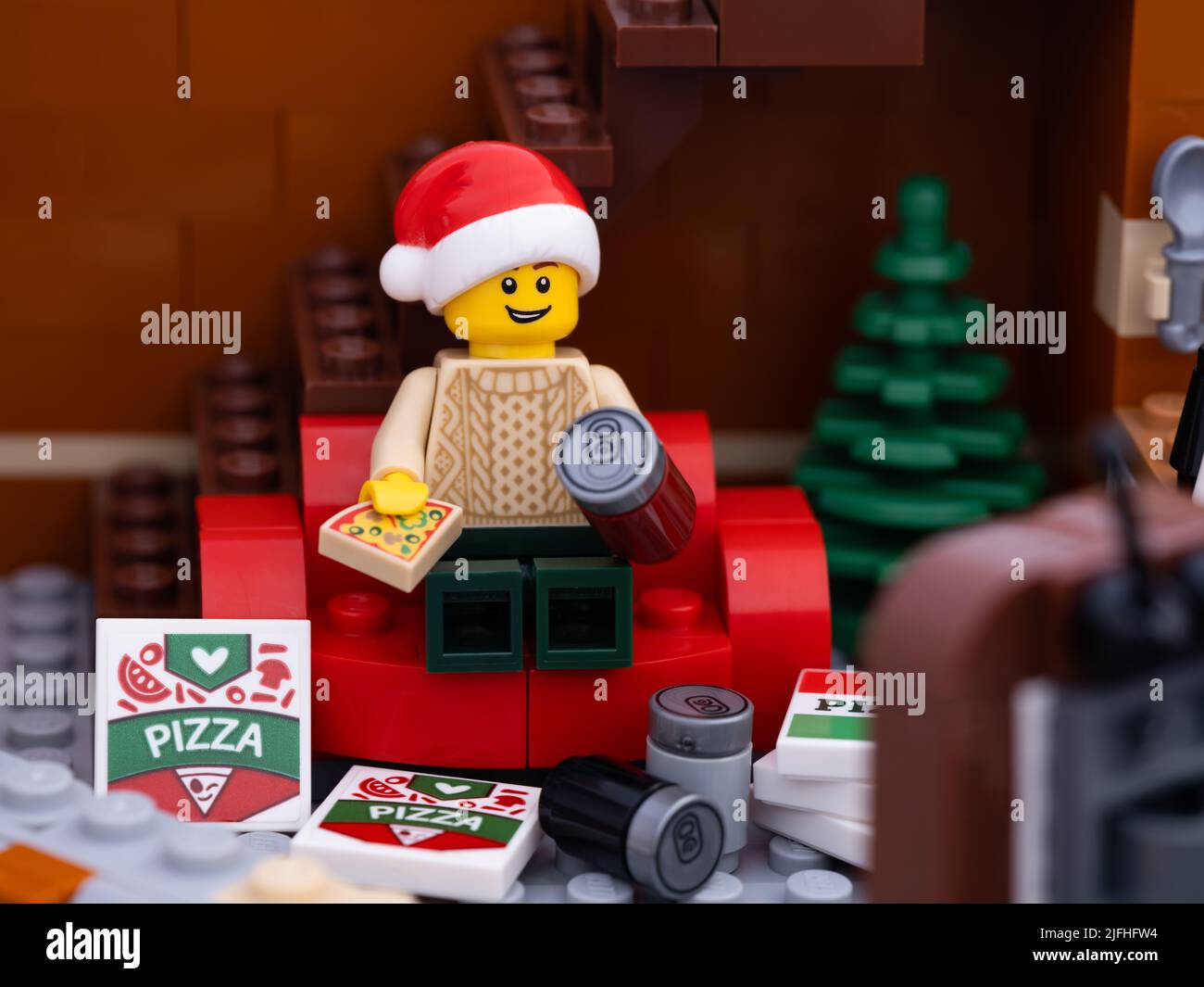Tambov, Russian Federation - January 03, 2022 A Lego man wearing a christmas hat sitting on a red couch eating a pizza and watching television with pi Stock Photo