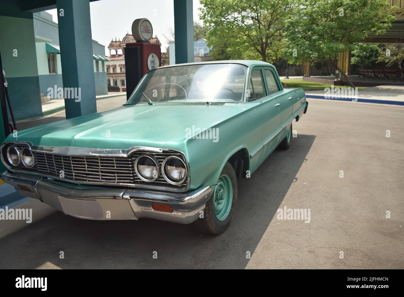 An Old Fashioned American Green colored car resembling Chevrolet  Impala parked near a petrol Bunk against a green background. It is a vintage Car Stock Photo
