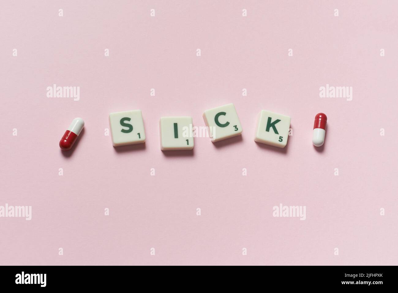 Sick word formed of scrabble blocks and pharmaceutical pills over pink