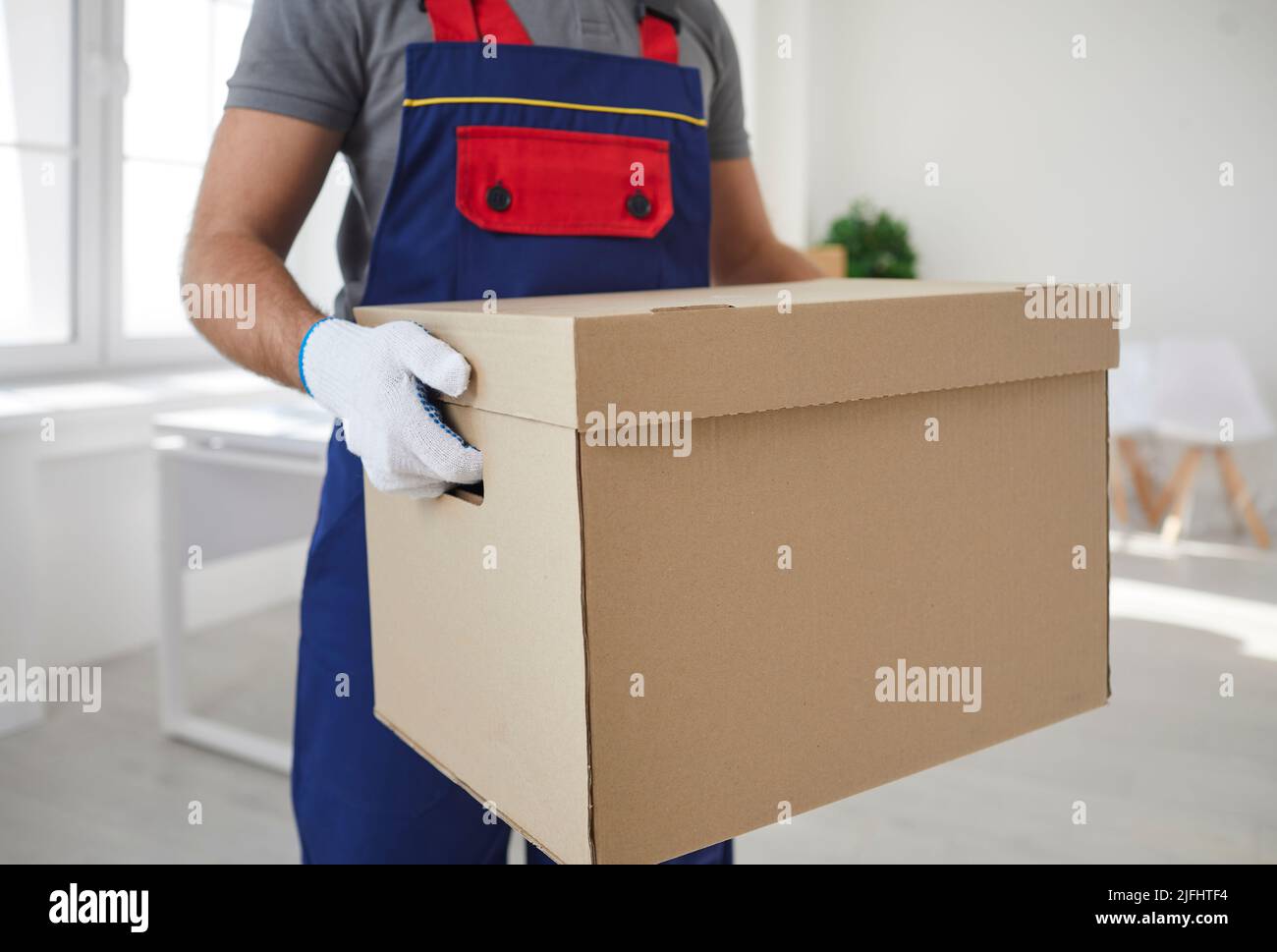Large cardboard box with things in hands of male employee of moving and delivery company. Stock Photo