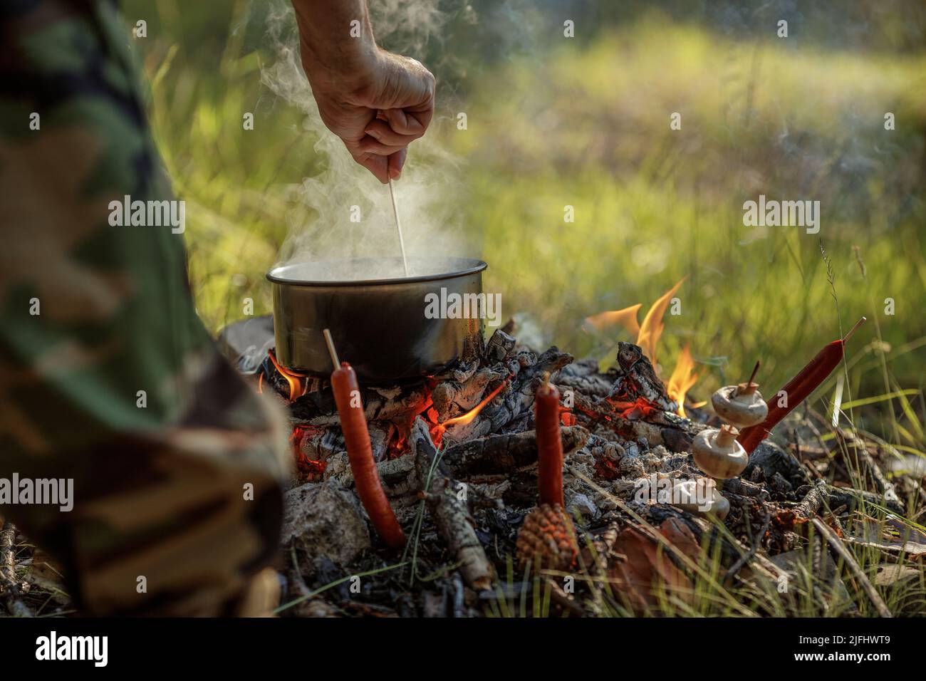 Cooking food in pot on campfire. The concept of adventure, travel, tourism, camping, survival and evacuation. Stock Photo