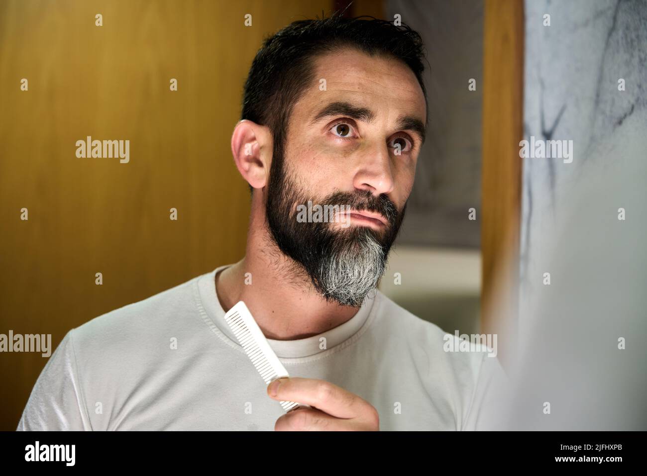Young man grooming and combing his beard with comb in front of mirror. High quality photo Stock Photo
