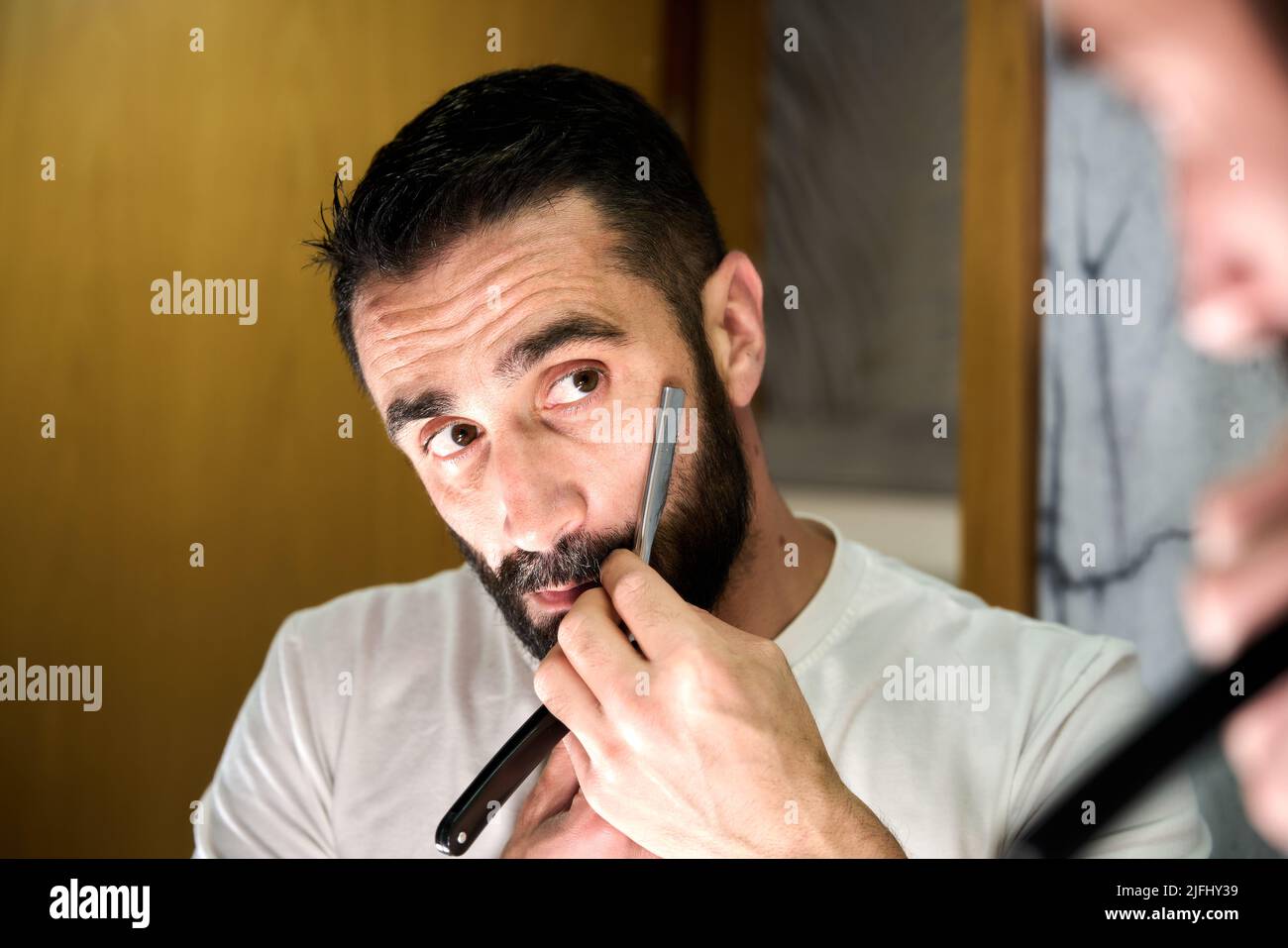 Young man with a beard shaving with a traditional knife in front of the mirror. High quality photo Stock Photo