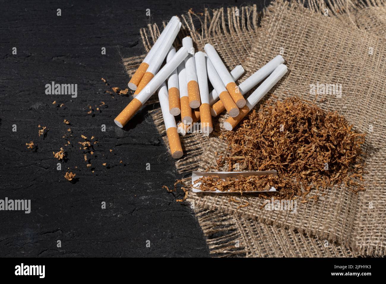Cigarette and smoking tobacco leaves on sackcloth background. Harmful