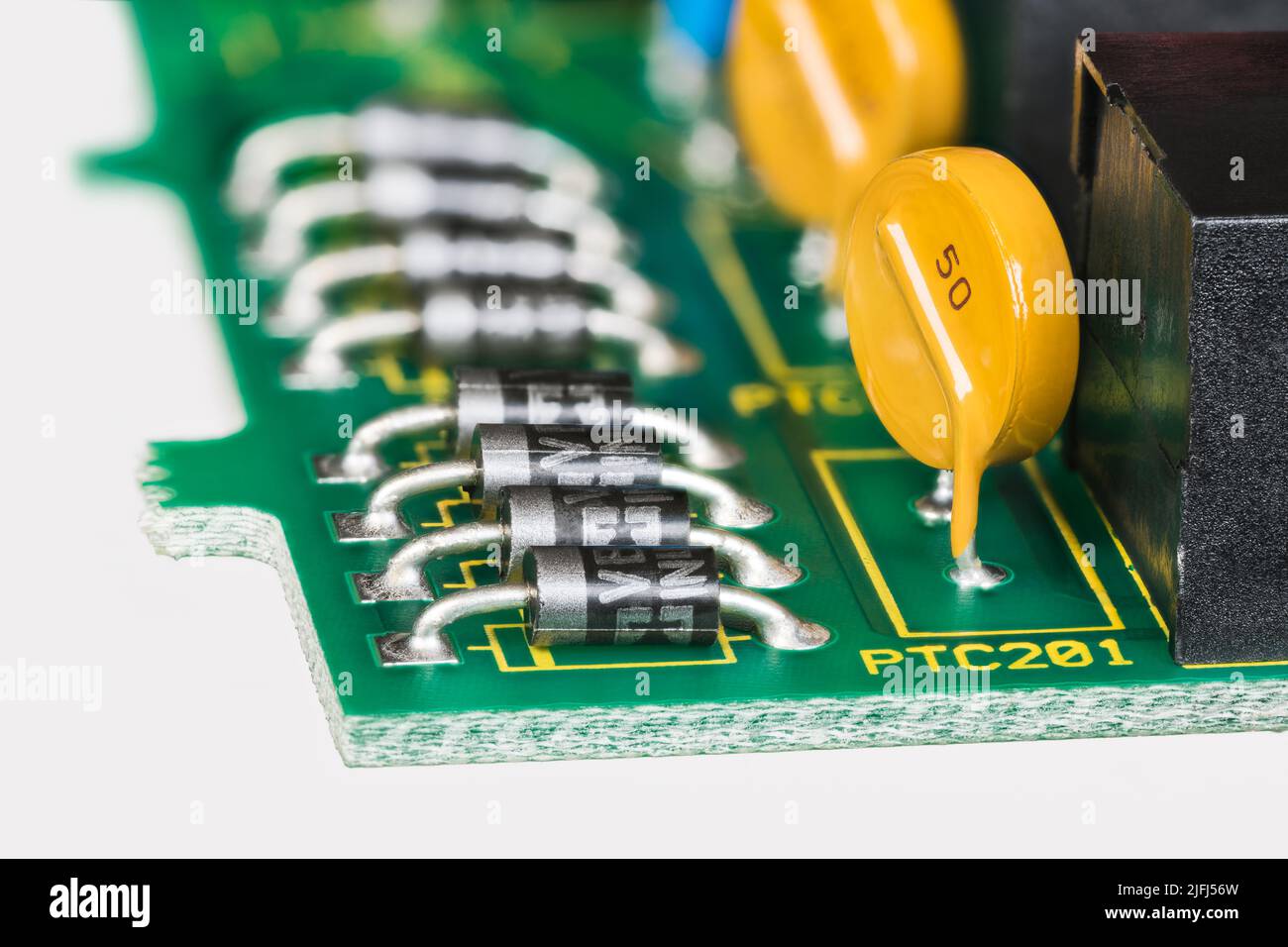 Semiconductor diodes and yellow resettable fuses in PCB detail on a white background. Closeup of electronic components on green printed circuit board. Stock Photo