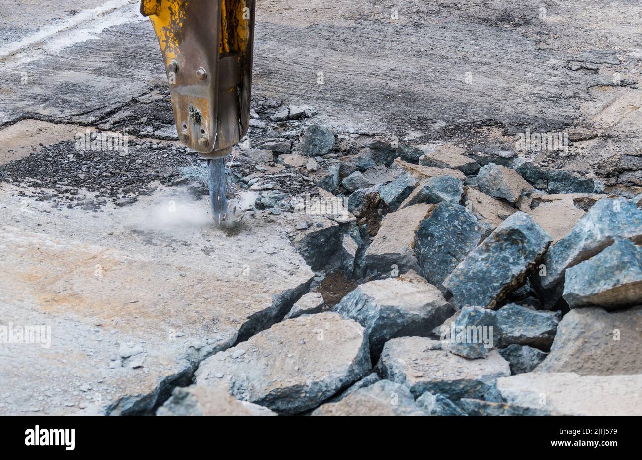 Close-up of demolition hammer with dust and sparks and broken concrete pieces. Detail of hydraulic jackhammer mounted on excavator arm. Repair working. Stock Photo