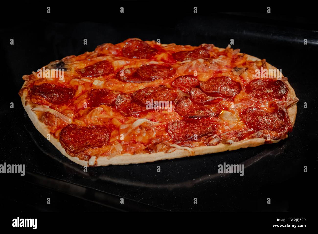 Burnt homemade pizza on tray in electric oven, black background Stock Photo
