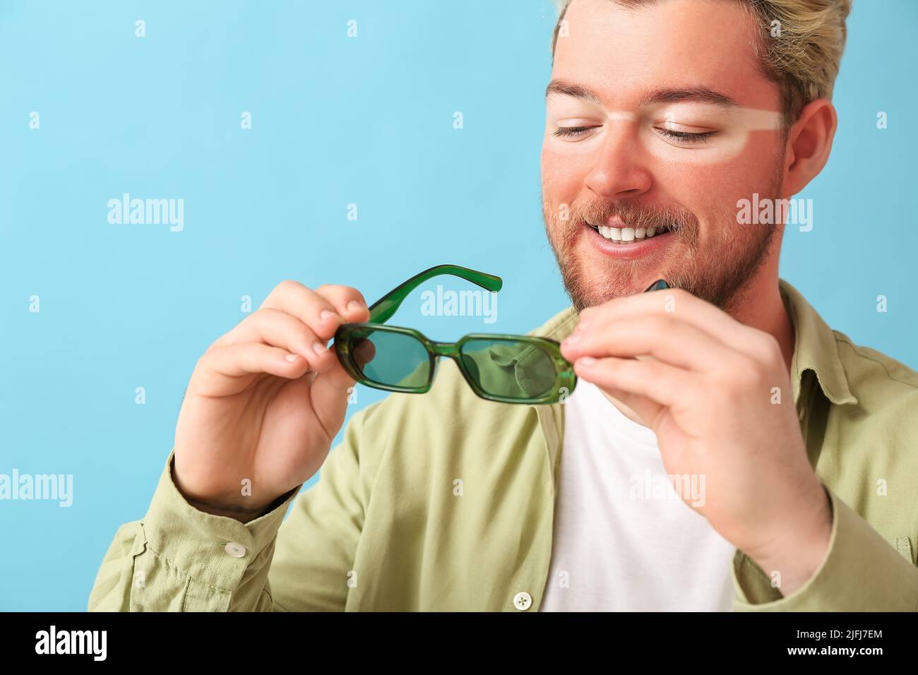 Happy young man with sun tanned skin and sunglasses on blue background Stock Photo
