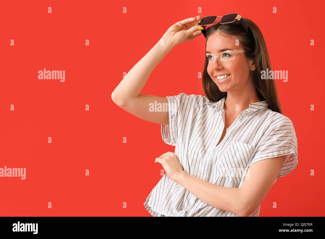 Happy young woman with sun tanned skin and sunglasses on red background Stock Photo