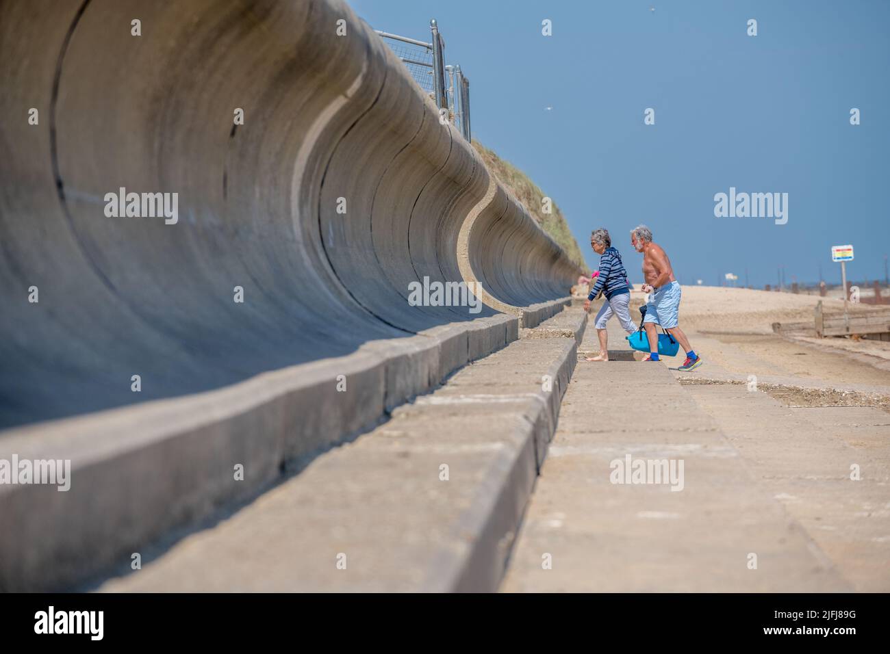 Elderly couple walking off the beach at Horsey Gap towards the concrete sea defences, Stock Photo