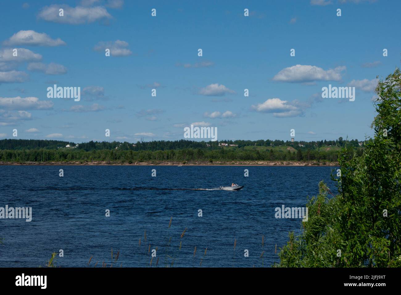 Deep cold ryokana in the north of Russia. The seasons are summer. A sandy beach with green bushes growing on it. White clouds in the blue sky - Stock Image