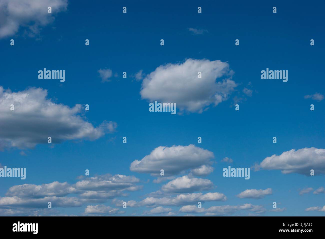 The horizontal photo is a blue sky with white fluffy clouds. Background, screensaver. Summer. Cloudy. Sunshine - Stock Image