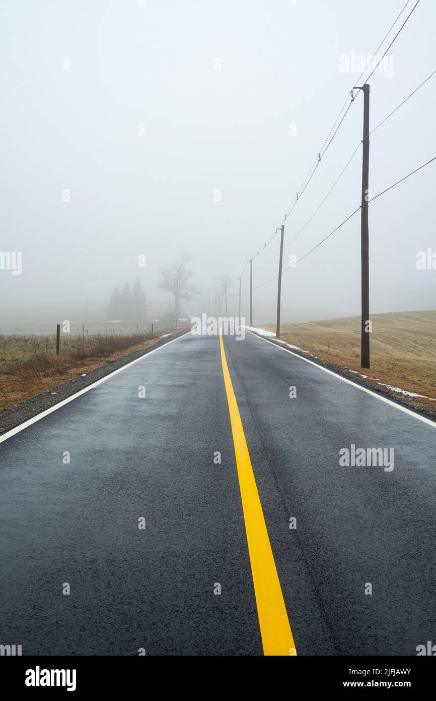 A foggy road with a bright yellow line running down the middle in Templeton, Massachusetts Stock Photo