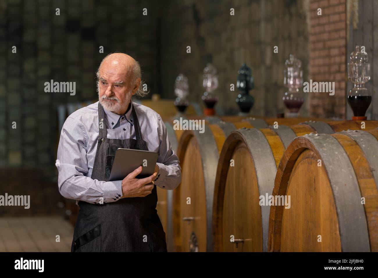 Senior man winemaker at winery checking barrels in wine cellar. Stock Photo