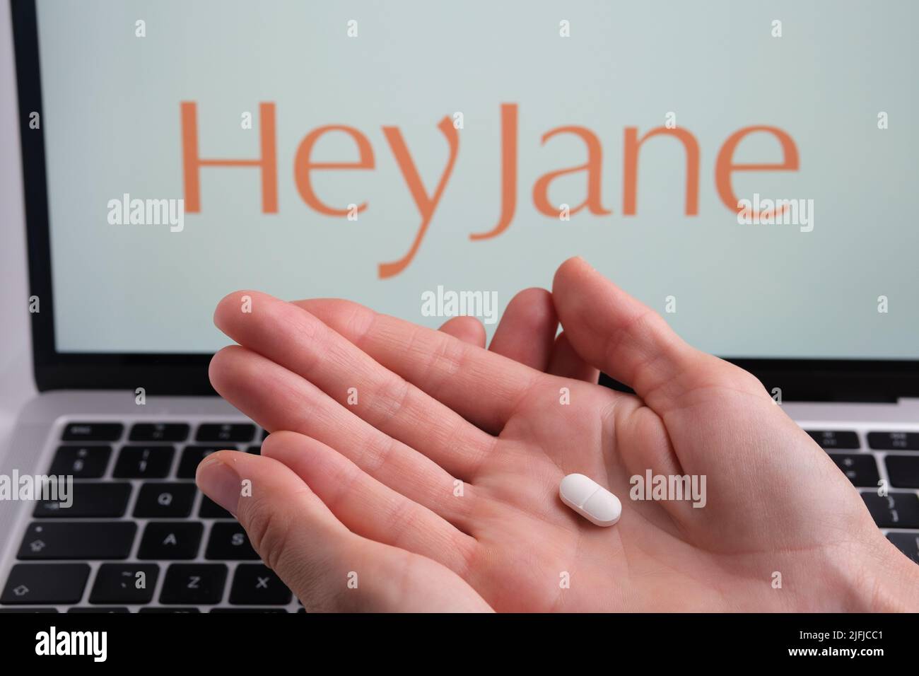 White pill in womans hand and Hey Jane company logo on a blurred background. Concept for online telehealth abortion platform. Stafford, United Kingdom Stock Photo