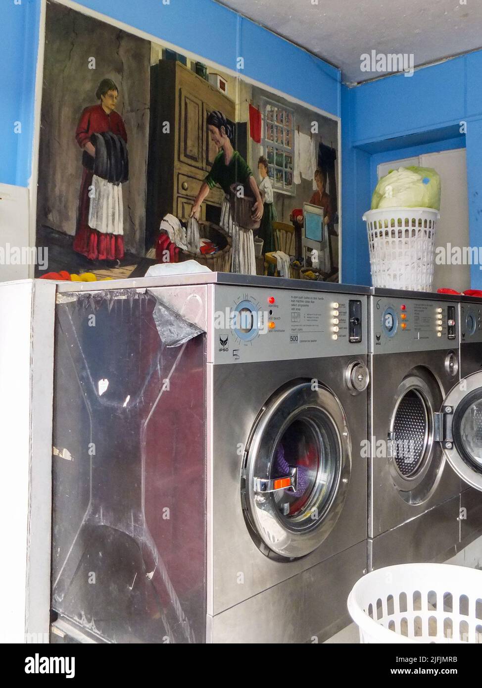A painting of women washing clothes contrasts with modern washing machines in a self-service launderette in Dublin, Ireland. Stock Photo