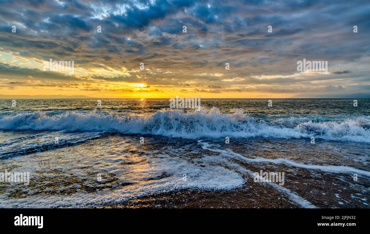 An Ocean Wave Is Breaking Against A Colorful Sunset Sky Stock Photo