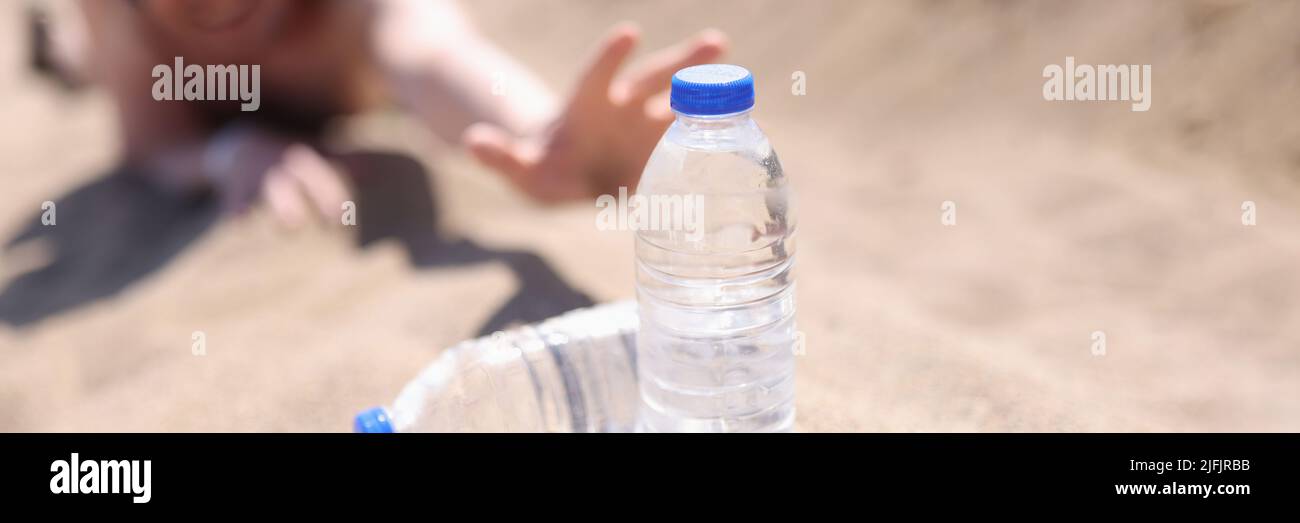 A man in the desert stretches on the sand for bottles of water Stock Photo