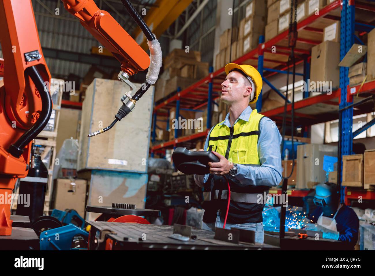 Worker man working with robot arm automate welding machine in modern metal factory. Engineer program robotic in heavy industry. Stock Photo