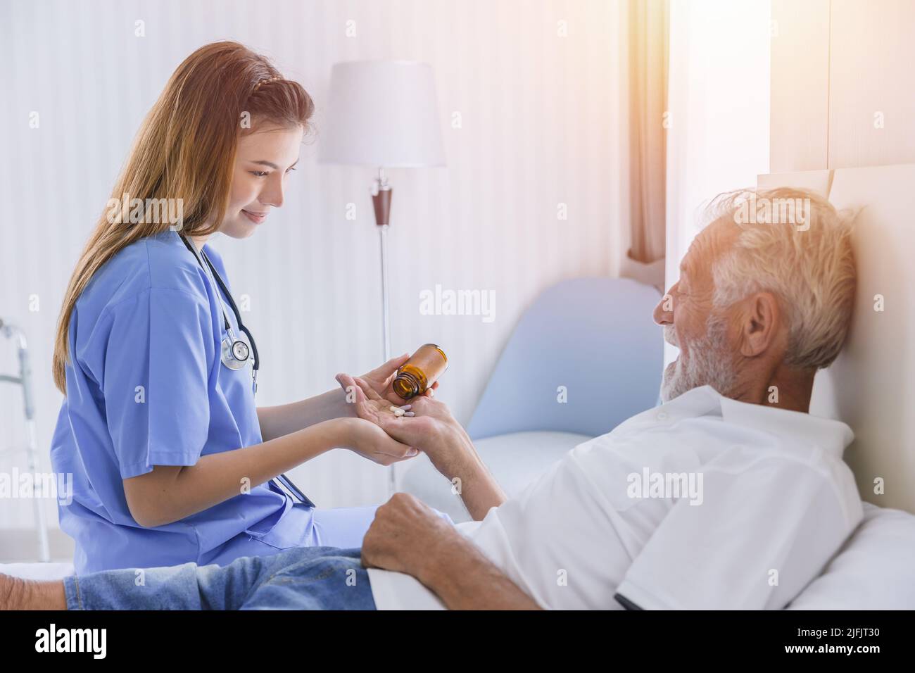 elderly man senior people lay on bed health care giving medicine pills from nurse at homecare Stock Photo