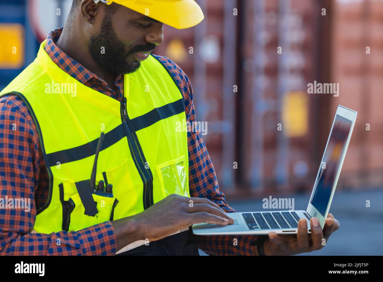 Port cargo staff worker using laptop computer online to manage control loading container in logistics industry. Stock Photo