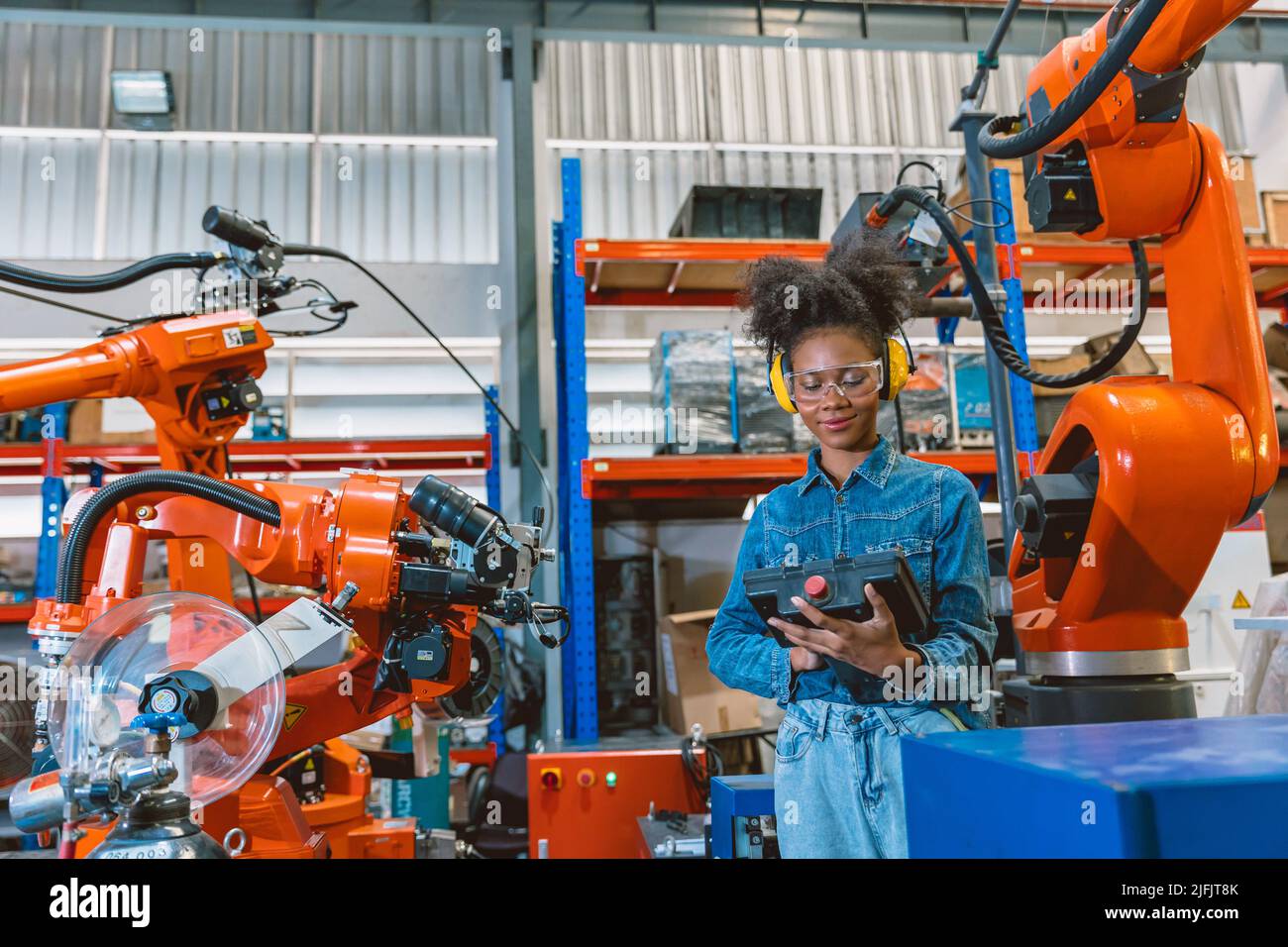 Engineer smart woman worker working programing robotic welding machine. Black teen girl work in advance modern factory. Stock Photo