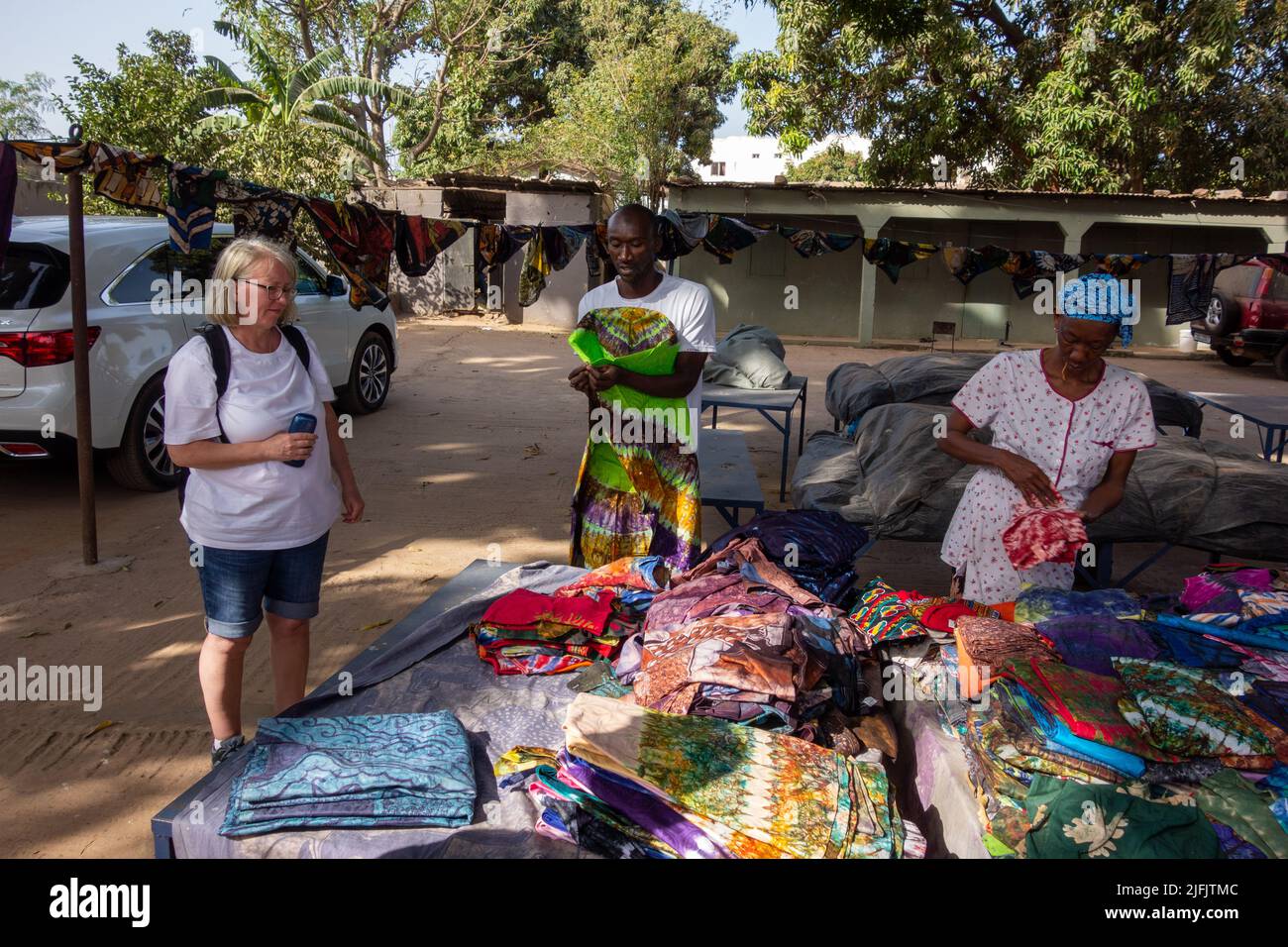 BAKAU, THE GAMBIA - FEBRUARY 6, 2022 Batik factory Gambian man and woman selling sloth to woman tourist Stock Photo