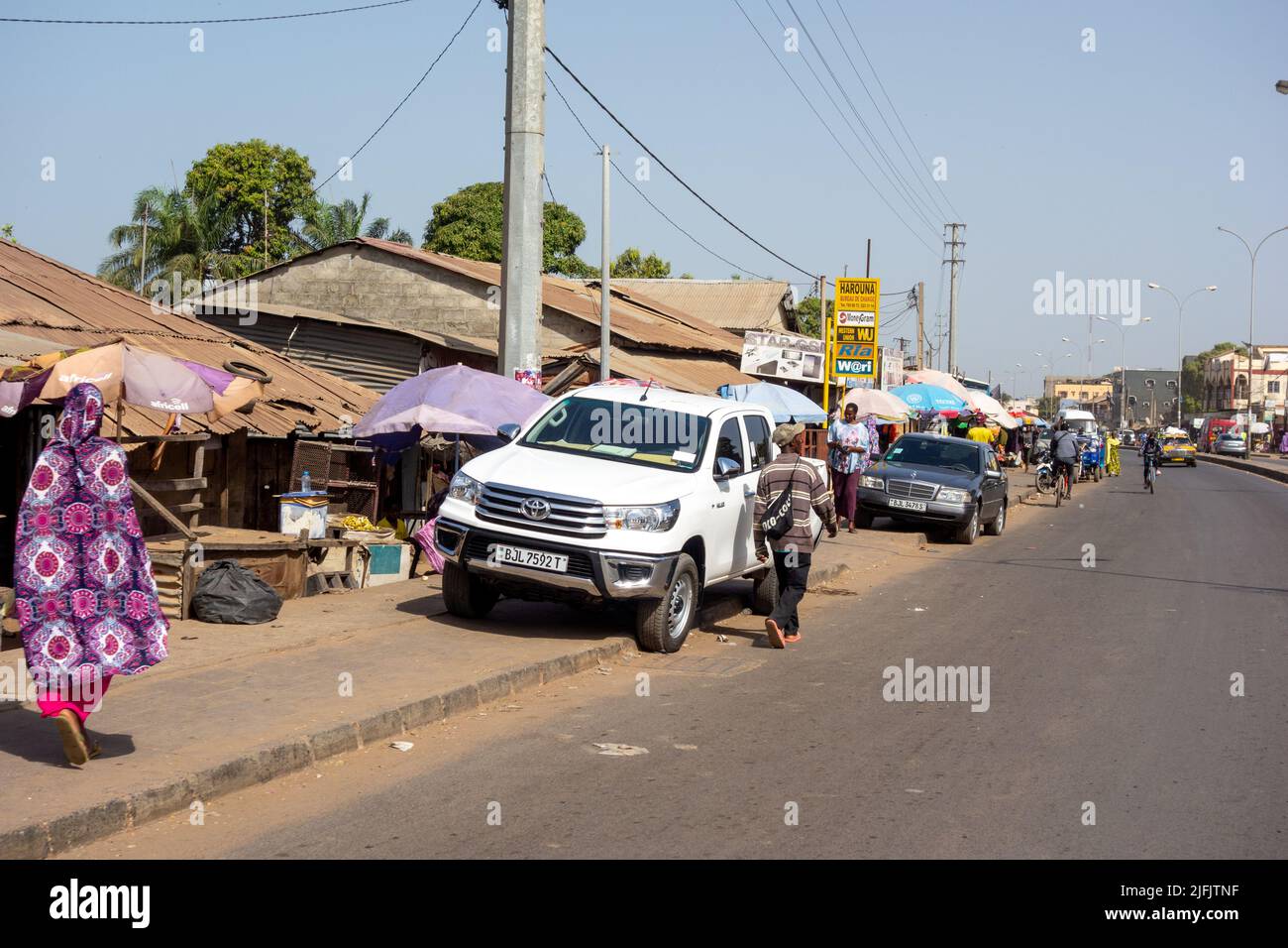 BAKAU, THE GAMBIA - FEBRUARY 6, 2022 cars and shoppers on the Old Cape Road Stock Photo