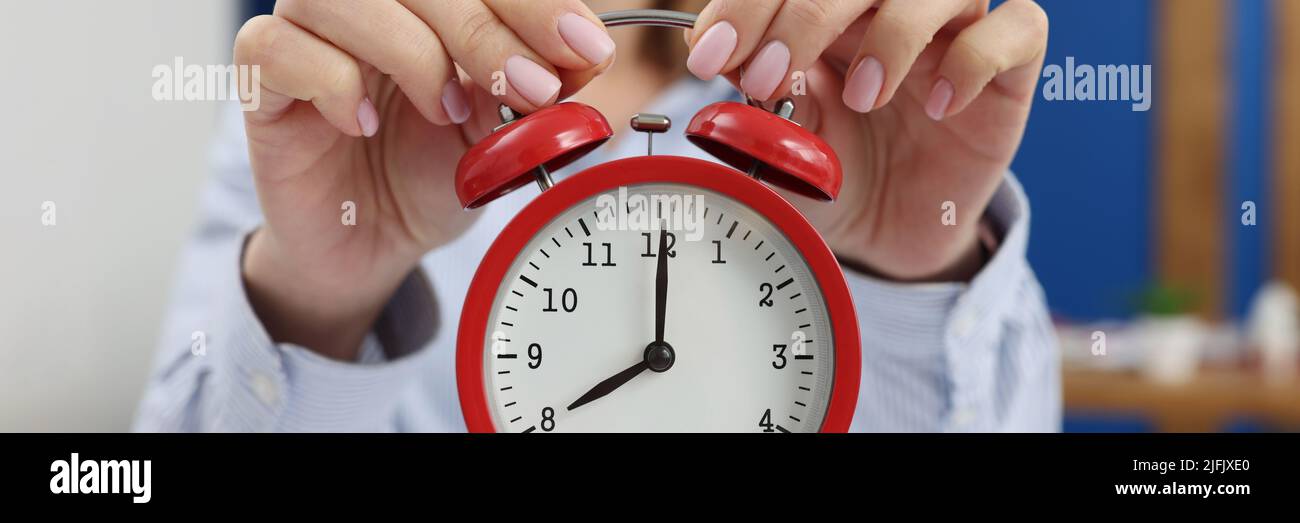 A woman at home holds a red alarm clock, close-up Stock Photo