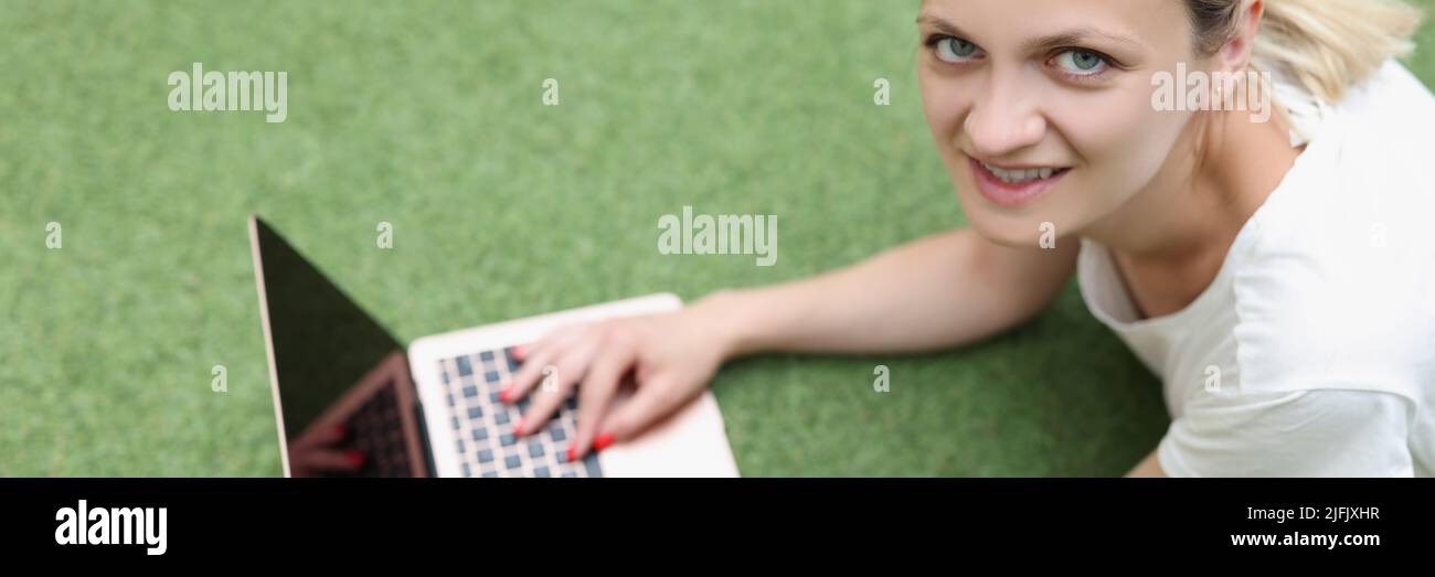 Young woman freelancer with laptop lies on green cover Stock Photo