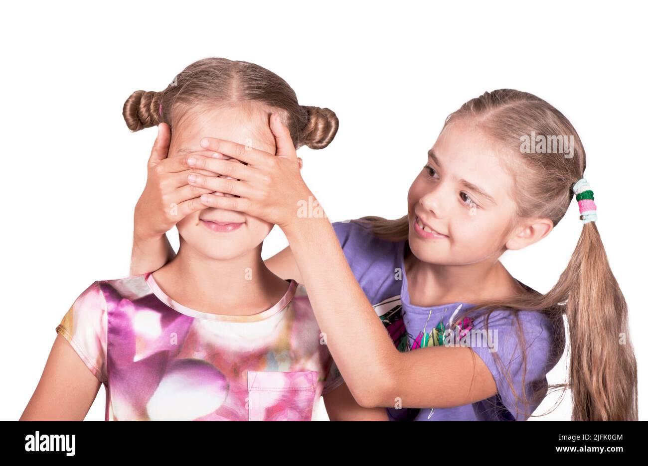 Children play and joke. One girl closes the eyes of another. Photo