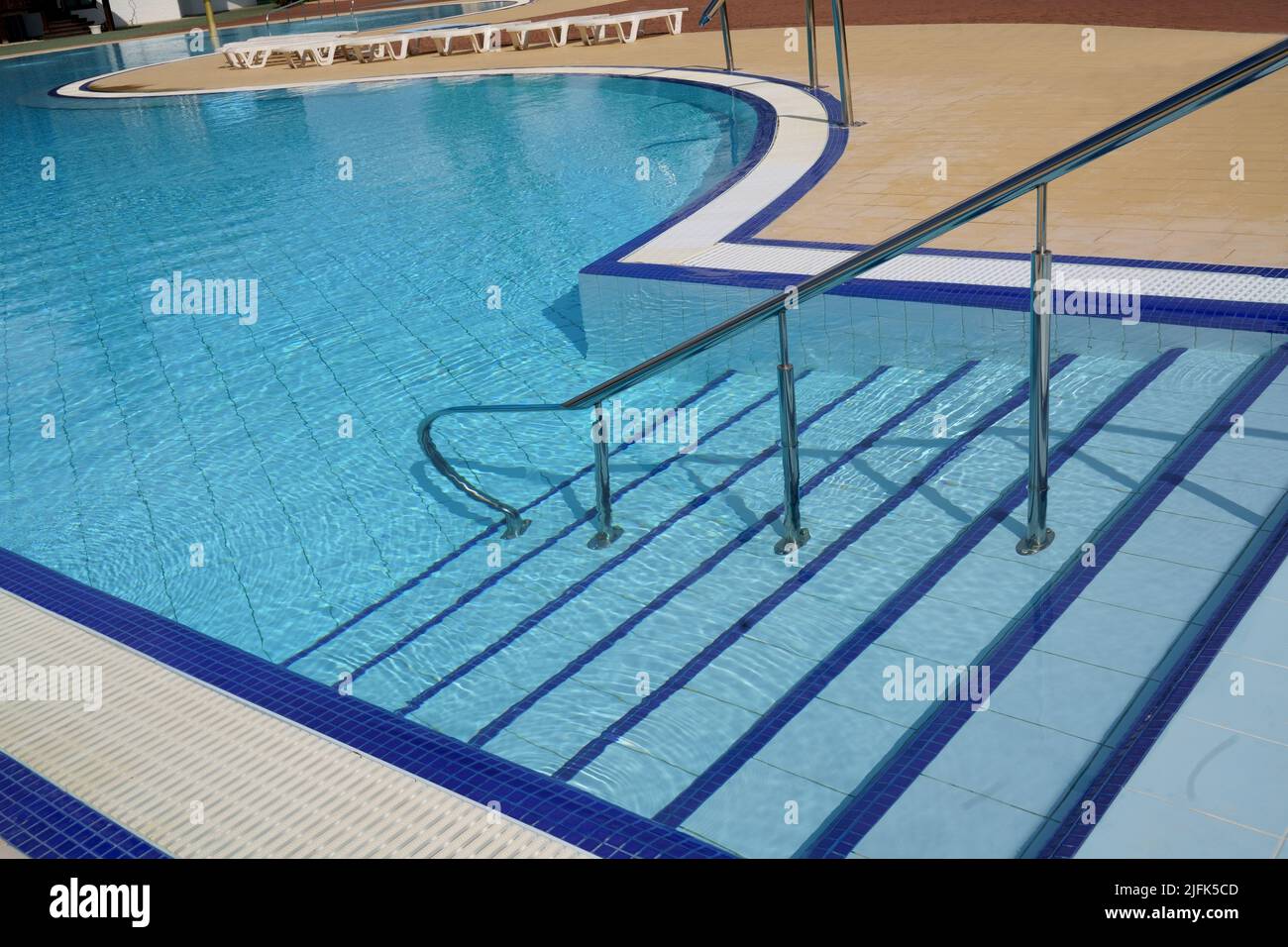 Railings and stairs going down the blue water of an outdoor swimming