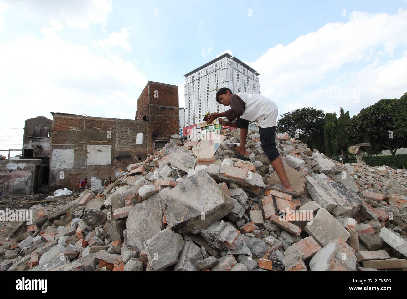 July 3, 2022, Jakarta, Jakarta Capital Special Region, Indonesia: Children play with kites in the rubble of a residential building burned down with heavy equipment and an apartment building as a background at the former site of a fire in the Kampung Pasar Gembrong area, East Jakarta, Indonesia. The Provincial Government of the Special Capital City Region of Jakarta has begun revitalizing residential areas in the former location of the fire in the Pasar Gembrong Village, East Jakarta, Indonesia. The Pasar Gembrong Village, which is called Kampung Gembira Gembrong, has a total of 136 buildings. Stock Photo