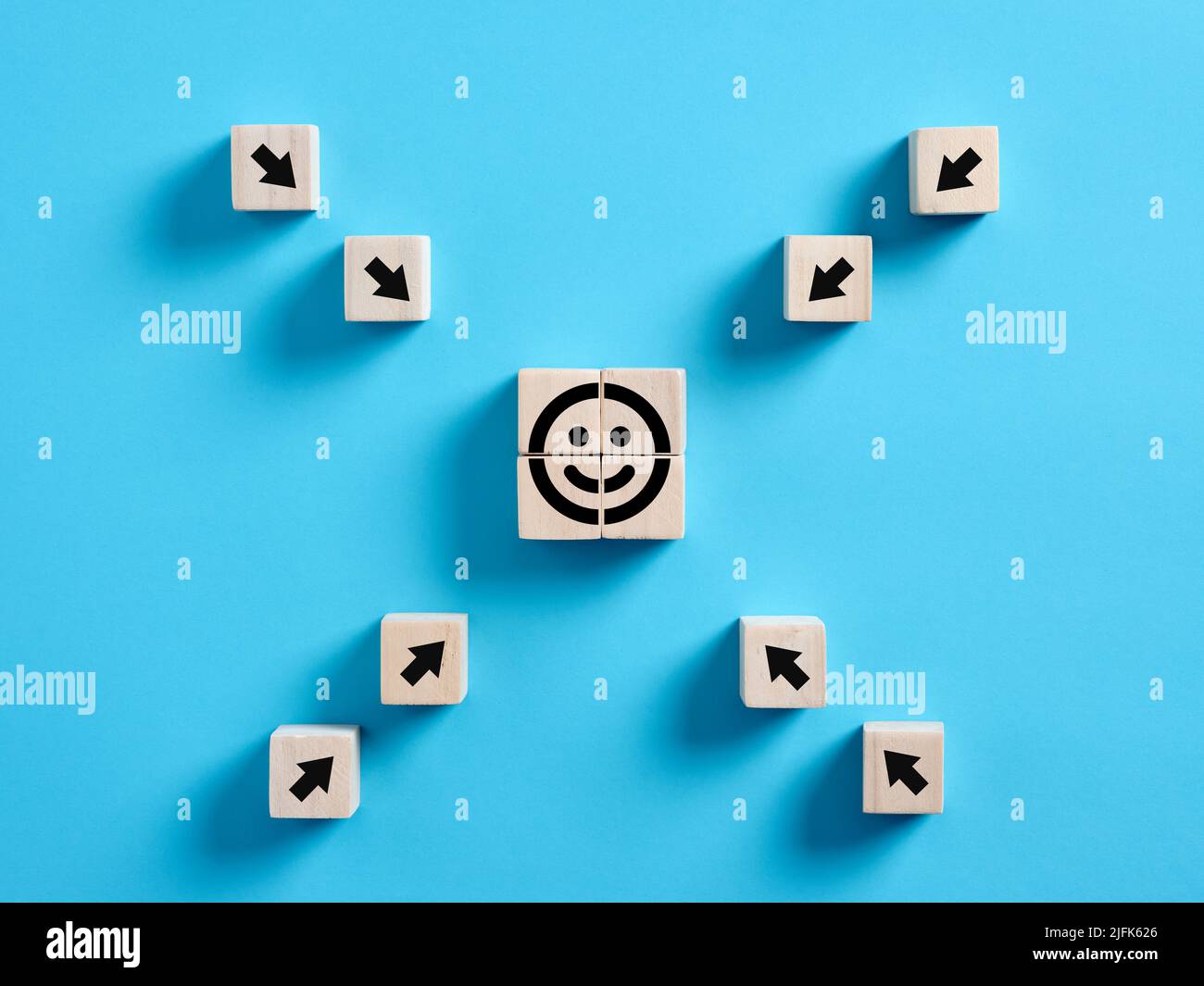 Arrows pointing towards the smiling face emoticon on wooden cube. Customer satisfaction, evaluation or happy client concept. Stock Photo