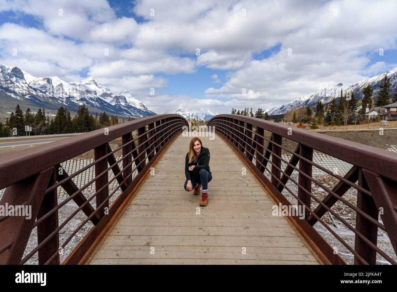 A middle aged woman sitting in the middle of a wood pedestrian bridge