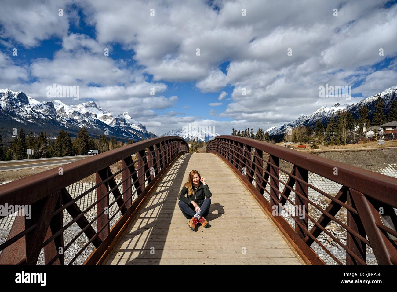 A middle aged woman sitting in the middle of a wood pedestrian bridge