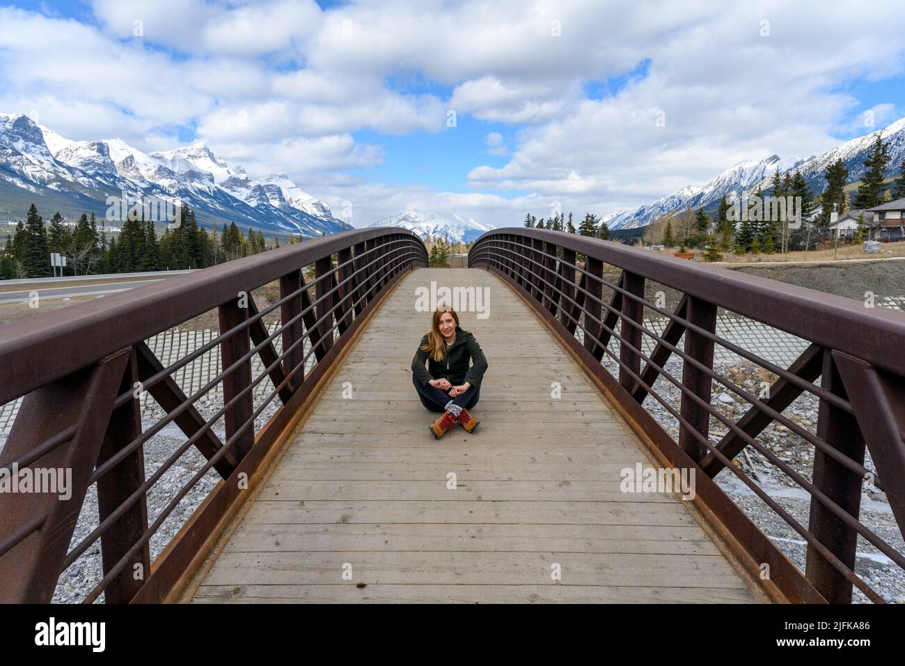 A Middle Aged Woman Sitting In The Middle Of A Wood Pedestrian Bridge