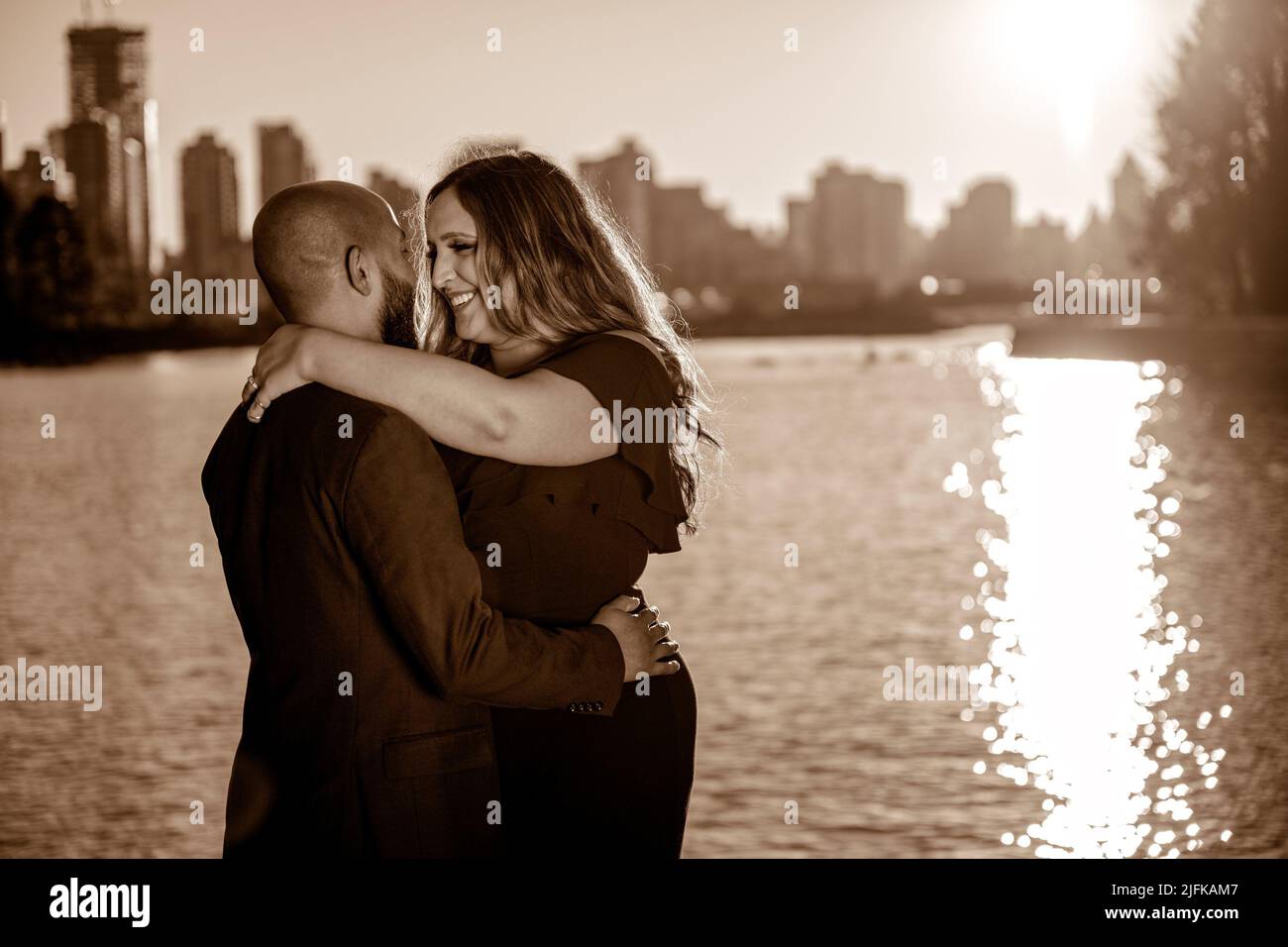 Emotional photo of a well dressed mixed race couple hugging and holding each other with skyscrapers in the background in Vancouver, British Columbia, Stock Photo