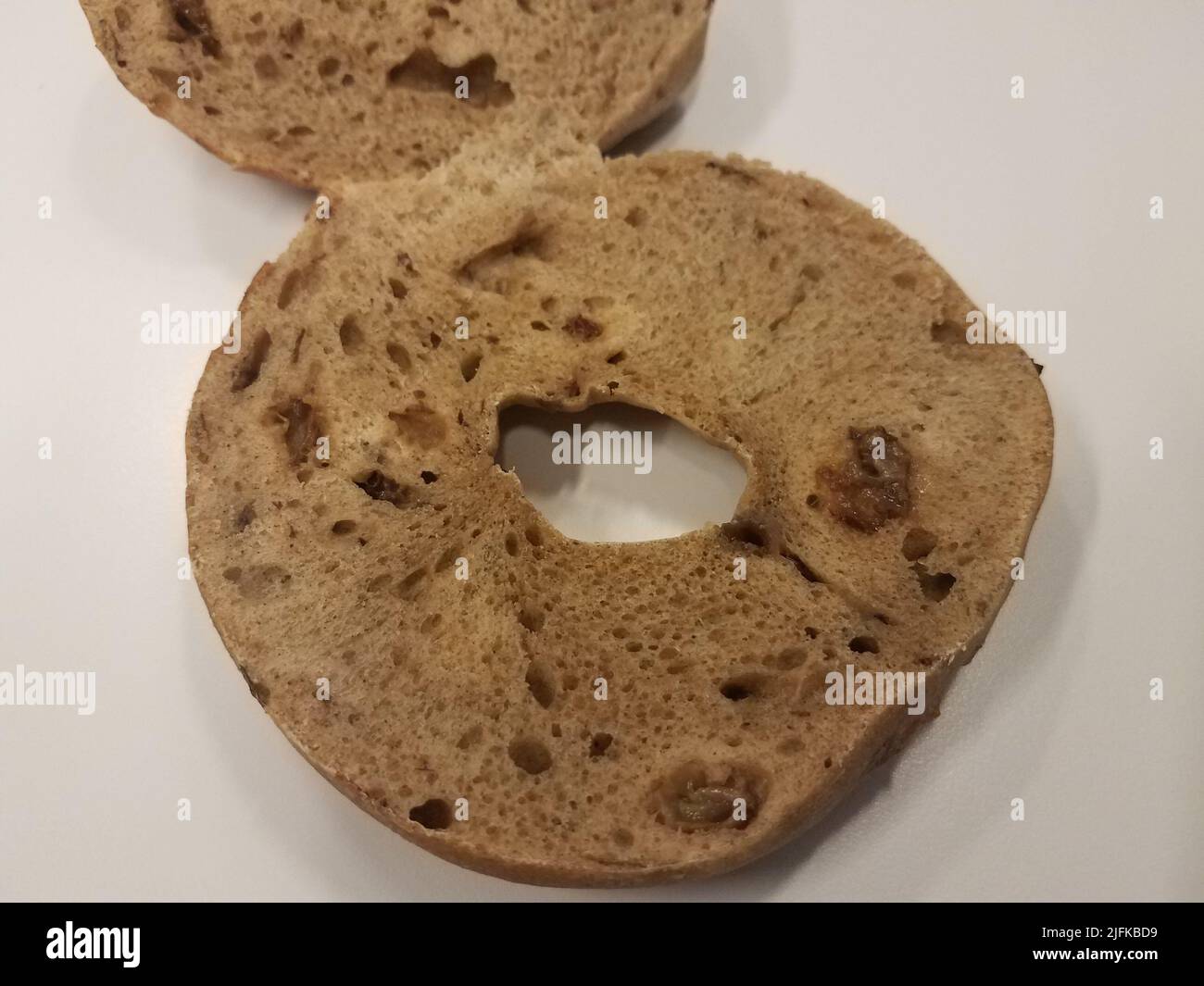 a raisin bagel sitting on a white surface sliced in half Stock Photo