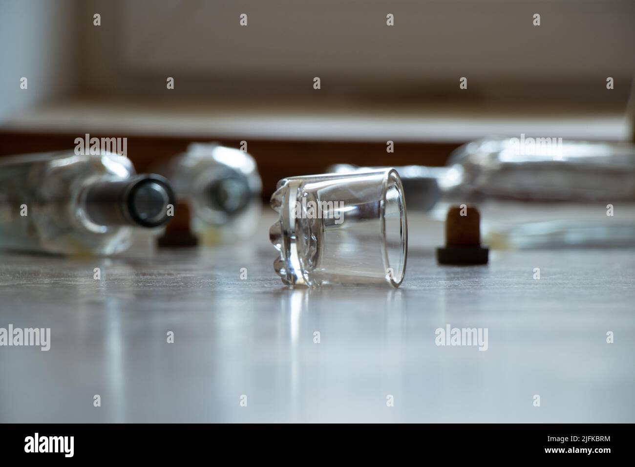 A glass and empty alcohol bottles lie on the floor in an apartment in the dark, alcoholism and bad habits, glass bottles and a glass of vodka Stock Photo