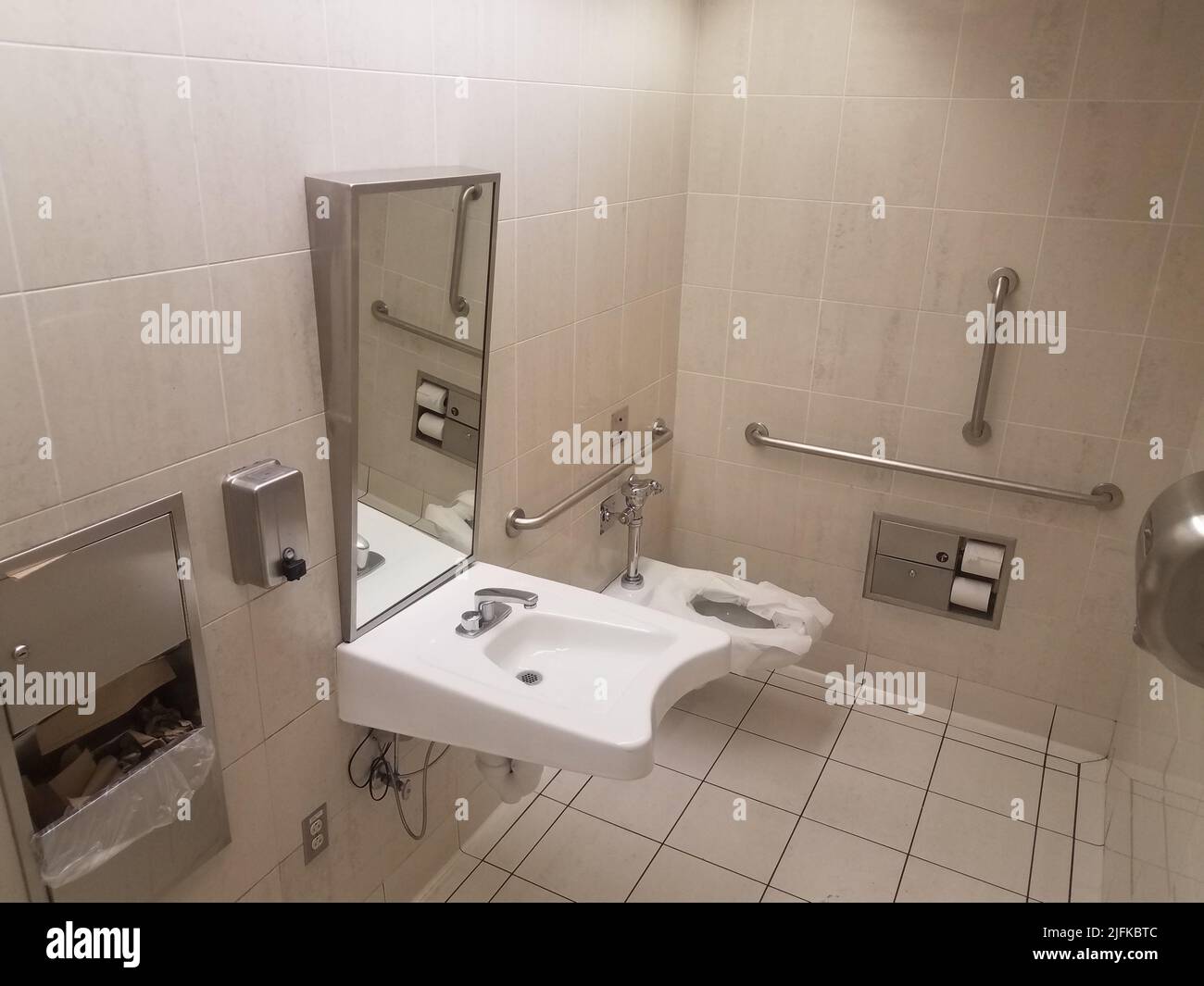 bathroom or restroom toilet with paper and metal railings and sink. Stock Photo