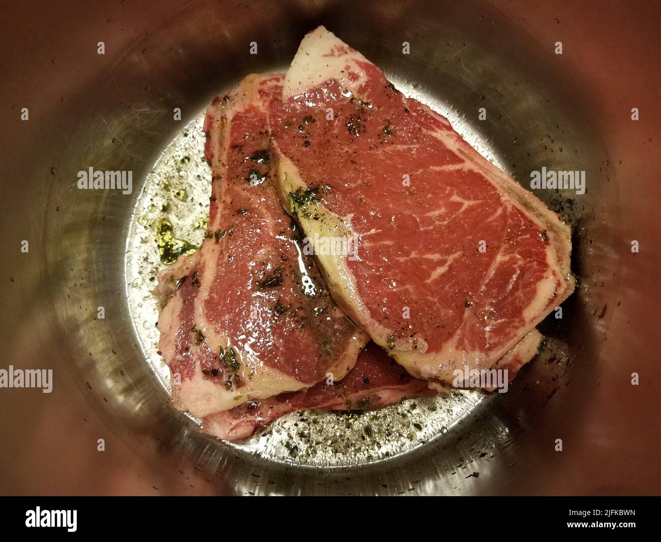 beef steak with seasoning and liquid in metal pot or container Stock