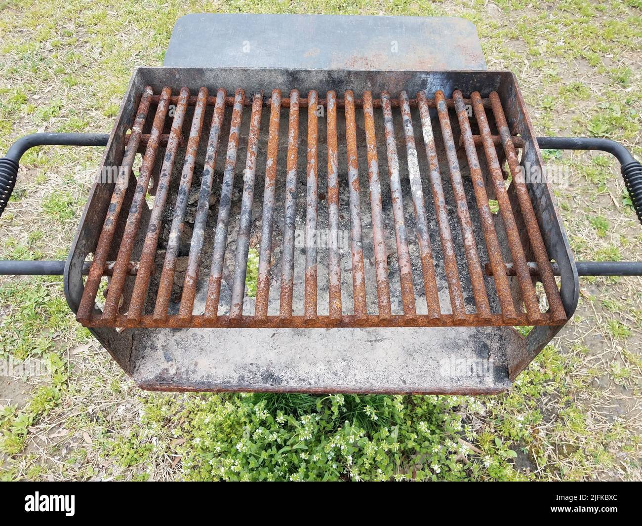 weathered and brown rusted metal bars on barbecue grill with soot and a hole. Stock Photo