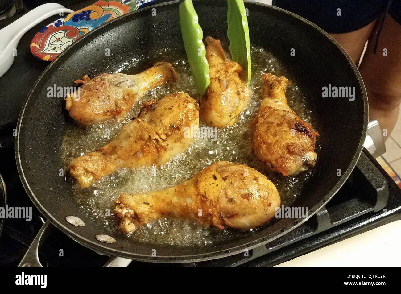 chicken drumsticks cooking in hot oil in frying pan on stove Stock